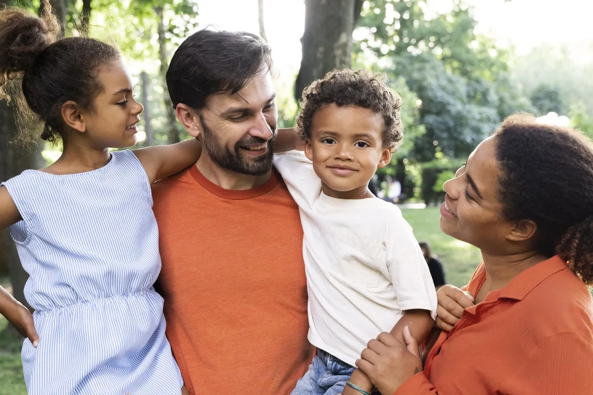 Pai, mãe e dois filhos abraçados num parque